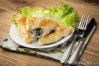 Puff pastry with spinach and feta (triangles) on the wooden background. Stock Photo