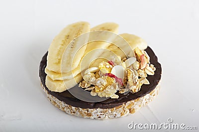 Puffed exploded wheat grains with chocolate glaze with muesli and cut banana slices on a light wooden background. Stock Photo