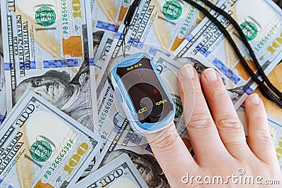 Pulse oximeter on fingers. Measurement of oxygen in the blood on the table near the dollars. Stock Photo