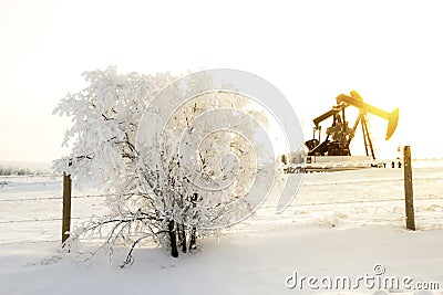 Pump jack in the sunrise light and the bush in snow in the oilfield Stock Photo