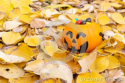Pumpkin basket for Halloween, full of candy on the background of yellow fallen leaves. Stock Photo