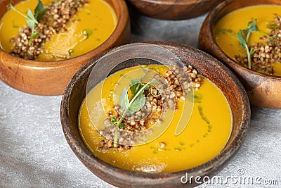 Pumpkin cream soup decorated with crunchy buckwheat in beautiful wooden plates. Stock Photo
