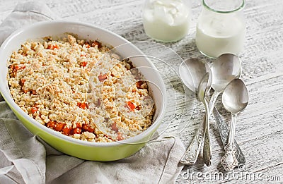 Pumpkin crumble in a ceramic baking dish and natural yoghurt in glass jars on a white wooden table. Stock Photo