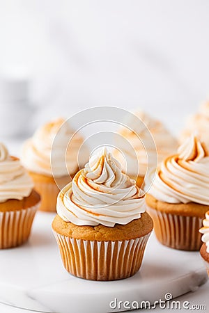 Pumpkin cupcakes on a white table topped with cream cheese frosting and dusted with cinnamon, generative AI Stock Photo