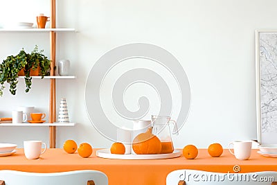 Pumpkin, oranges, mugs and jars on the dining room table covered with orange tablecloth. White empty wall with copy space Stock Photo