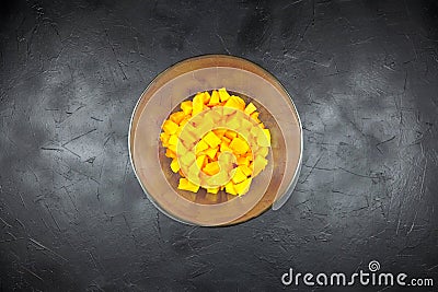 Pumpkin pieces in a round deep transparent glass bowl on black table, top view. Chopped pumpkin butternut squash in salad dish Stock Photo