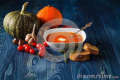 Pumpkin soup in a bowl with fresh pumpkins, garlic and parsley h Stock Photo