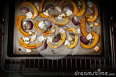Pumpkin or squash slices with red onions, garlic, feta cheese and thyme on a baking tray in the oven, autumn vegetable meal for Stock Photo
