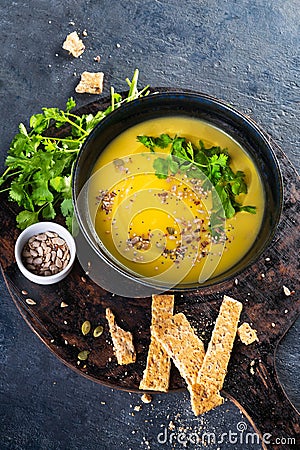 Pumpkin and vegetables cream soup with pumpkin seeds, slices of bread and parsley over a dark background with Space for text. Stock Photo