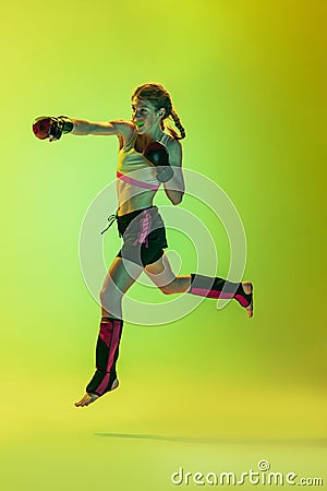 Dynamic portrait of athletic girl, MMA fighter training isolated on gradient yellow-green background in neon. Concept of Stock Photo