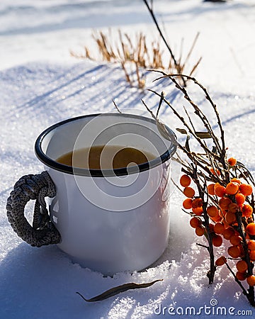 Punch with sea buckthorn berries in an iron white mug in the snow. Sea buckthorn twigs with tea Stock Photo