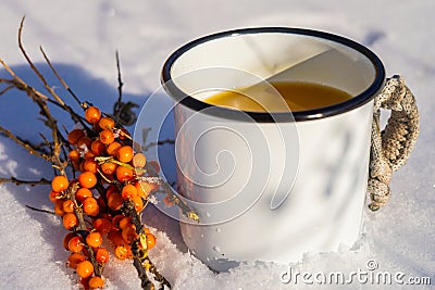 Punch with sea buckthorn berries in an iron white mug in the snow. Sea buckthorn twigs with tea Stock Photo