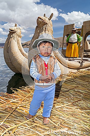 Puno, Peru - circa June 2015: Small boy in traditional clothes and canoe boat at Uros floating island and village on Lake Titicaca Editorial Stock Photo