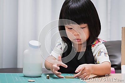 Pupil girl doing paper craft at homeschool. Kindergarten student gluing. Happy child wearing black apron. Baby aged 4-5 years old Stock Photo