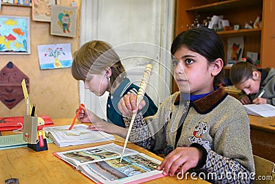 Pupil girl of initial classes meets lesson in rural school. Editorial Stock Photo