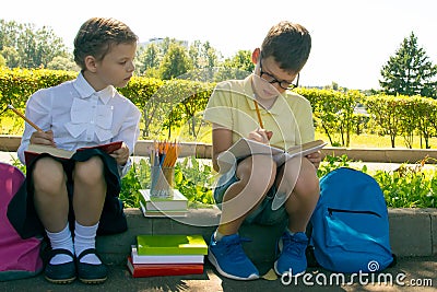 Pupils, a boy and a girl, doing tests of the school program, in the park outdoors, holding pencils Stock Photo