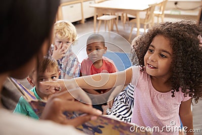 Pupils At Montessori School Looking At Book With Teacher Stock Photo