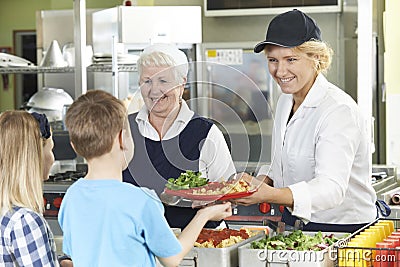 Pupils In School Cafeteria Being Served Lunch By Dinner Ladies Stock Photo