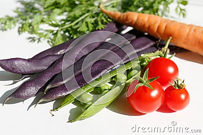 purple beans in pods, green peas in a pod, red cherry tomatoes, greens and raw carrots Stock Photo