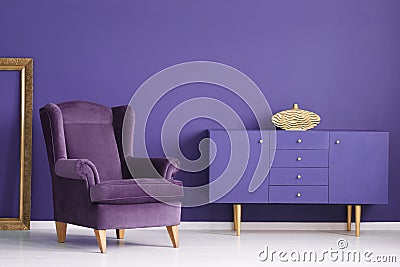 Purple cabinet with a golden vase, comfy armchair and frame in a Stock Photo