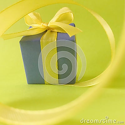 Purple gift box at the end of the spiral yellow ribbon, green background, square. Stock Photo