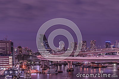 Purple night on circular highway leading to the Rainbow Bridge with Cargo and cruise ships moored or sailing in Odaiba Bay of Editorial Stock Photo