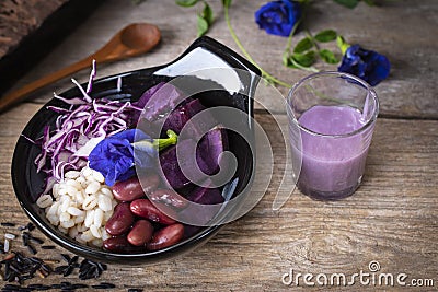 Purple vegetable salad in black bowl placed on the wood table there are spoon, black rice, salad dressing and flower placed around Stock Photo