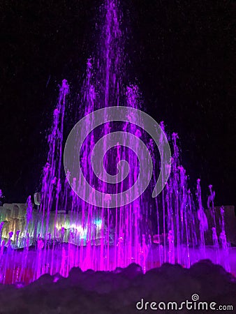 Purple water fountain and multi-colored lighted icicle walls in ice castle Stock Photo