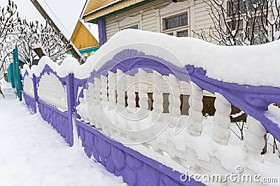 Purple and white concrete carved fence covered with snow, village house, snowy winter Stock Photo