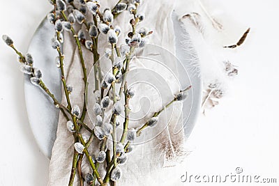 Pussy willow branches and feathers on modern plate on napkin on white wooden table. Top view. Modern Easter table decoration. Stock Photo