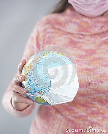 Putting a green surgical face mask on the globe sphere model. Heal the world from coronavirus covid-19 concept Stock Photo