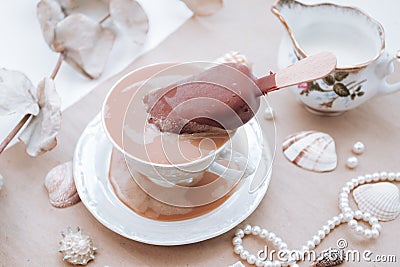 Putting ice cream in her morning coffee. Vintage porcelain mug, vintage decor, seashells and beads on the table Stock Photo