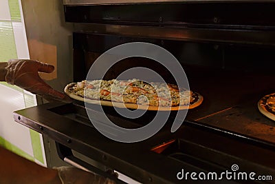 Putting seafood pizza into oven Stock Photo