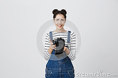 Puzzled confused brunette female photographer with two hairbuns wearing denim overall using modern camera. Woman with Stock Photo