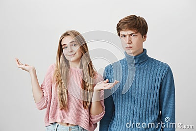 Puzzled confused young couple, female in pink sweater shrugging shoulders, saying so what, not feeling guilty. Frowning Stock Photo