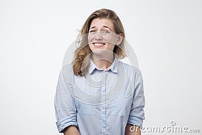 Puzzled female dressed in blue shirt, clenches white teeth in confusion, shrugs shoulders as does not know answer Stock Photo