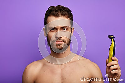 Puzzled handsome man looks embarrassed at electric shaver Stock Photo