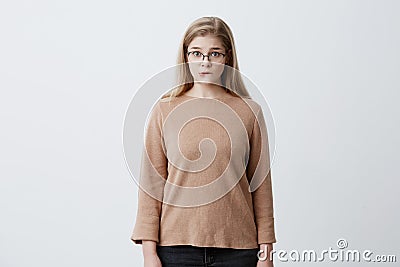 Puzzled pretty woman wearing eyeglasses with straight blonde hair biting her lower lip looking with surprise into camera Stock Photo