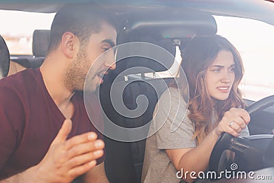 Puzzled young female driver trainee drives car, listens attentively male instructor who gives some advice, shows how to do it righ Stock Photo