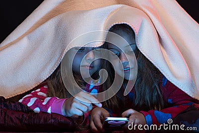 Pyjamas party for children: girls under blanket playing with phone Stock Photo