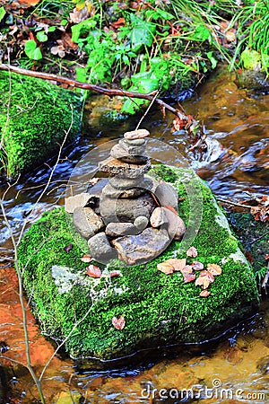 A pyramid of flat round stones stands on a large stone in the middle of a mountain rapid river Stock Photo