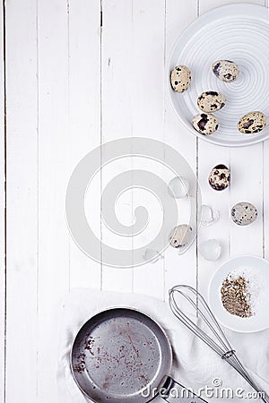 Quail eggs in a plate, a shell, a whisk for beating and a frying pan on a white wooden background. view from above Stock Photo