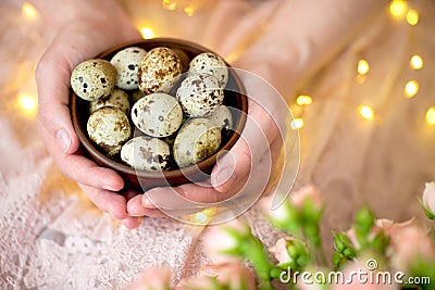 Quail eggs in a wooden plate in the hands of a girl on a pink background. Stock Photo