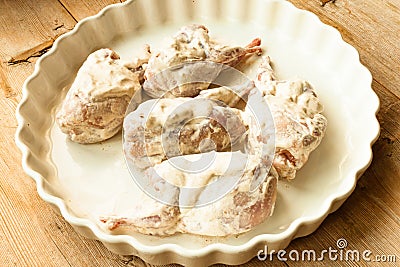 Quails plucked raw ready for cooking in sour cream on white plate on wooden background close up Stock Photo