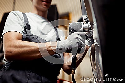 A qualified young mechanic changing a tire of a lifted car. Repair workshop Stock Photo