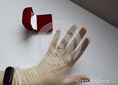 Quarantined wedding.coronavirus wedding.hand in a medical glove with a wedding ring on a white background next to a red Stock Photo