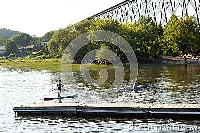 Woman on paddle board and man in kayak moving into the Cap-Rouge River from the St. Lawrence River Editorial Stock Photo