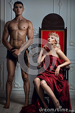 Queen sitting on a throne. Nearby is an athletic slave. Stock Photo