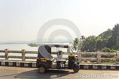 Indian rickshaw taxi stands on a bridge against the background of the river and green palm juggles Editorial Stock Photo