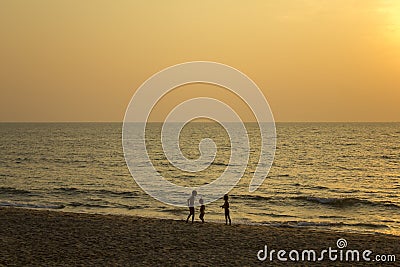 three dark silhouettes of children on the yellow sand of the beach against the sea and the evening Editorial Stock Photo